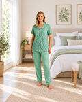 A woman stands barefoot in a bright bedroom wearing a mint green short-sleeve pajama top with a small floral print and matching long pajama pants.